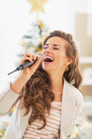 sretna mlada žena koja pjeva ispred božićnog drvca