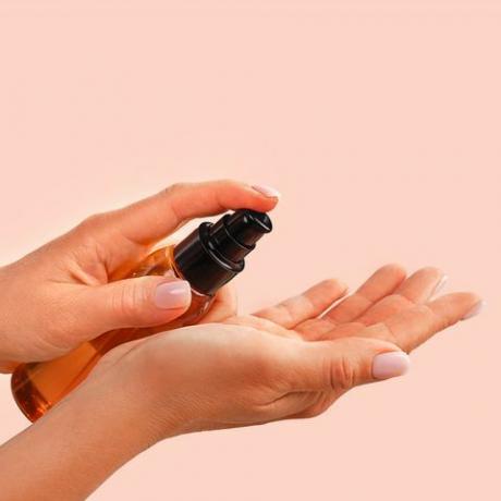 ženske ruke drže bočicu s prirodnim organskim serumom za lice ili eteričnim organskim uljem na trendovskoj pozadini ružičaste boje breskve